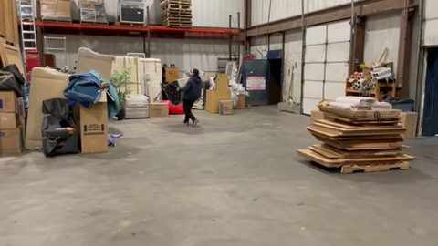 mover carrying a wrapped mattress across a storage warehouse