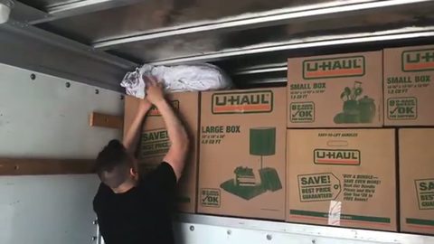 mover placing a wrapped bundle atop a wall of moving boxes in a truck